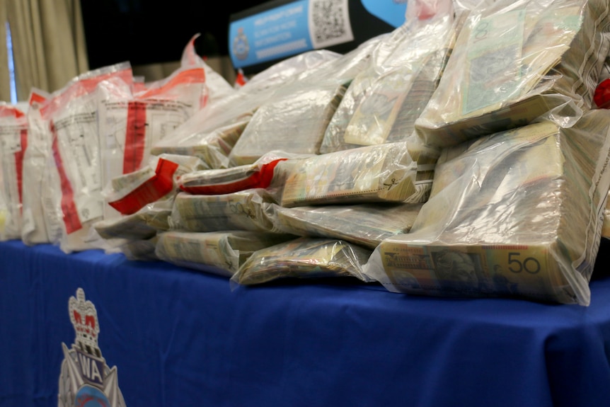 Stacks of $50 notes sit in plastic evidence bags on a table.