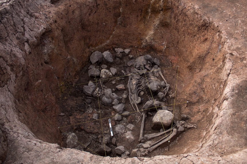 A big hole in the ground with rocks, ancient pottery and bones at the bottom with marking yellow string on top