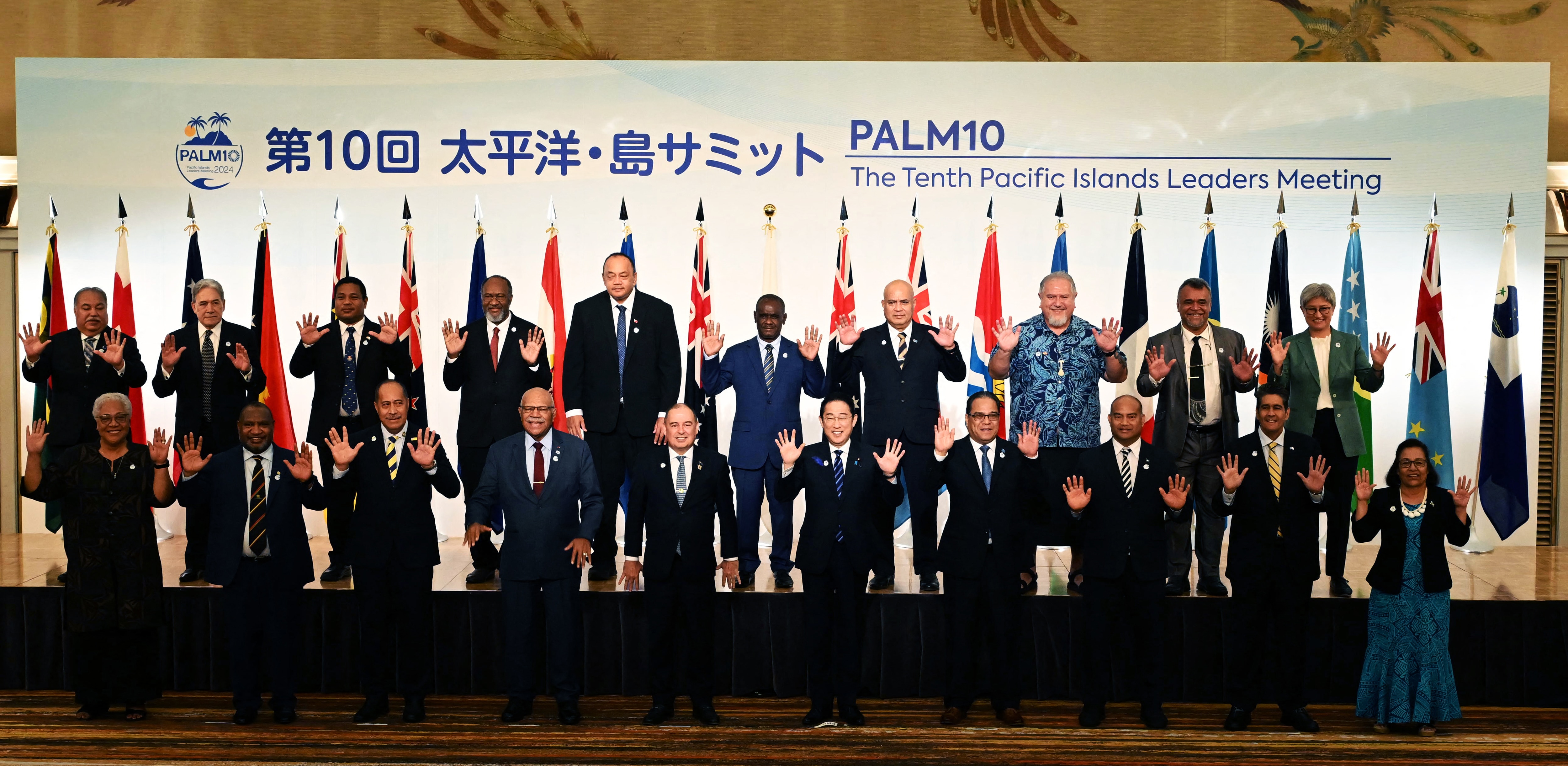 Two rows of men and women pose for a photograph with hands raised.