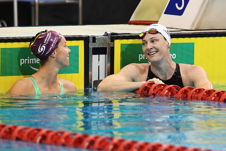 Two women in swimming caps look at each other while in water at end of swimming pool