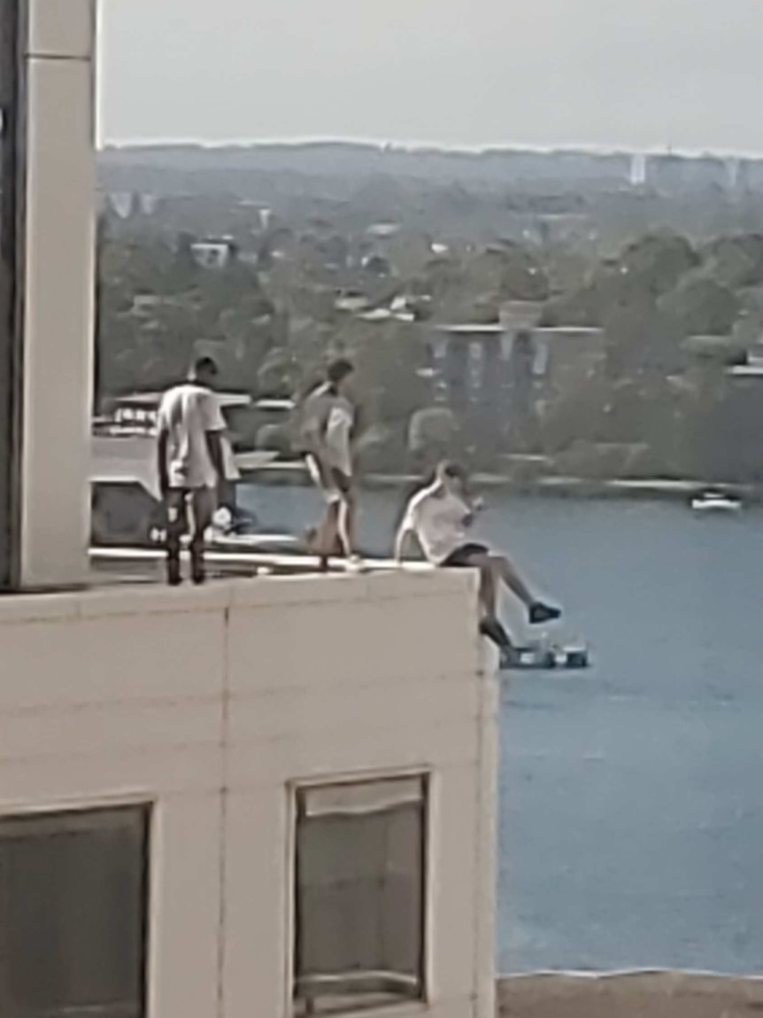 One male sits on edge of building, others stand behind him