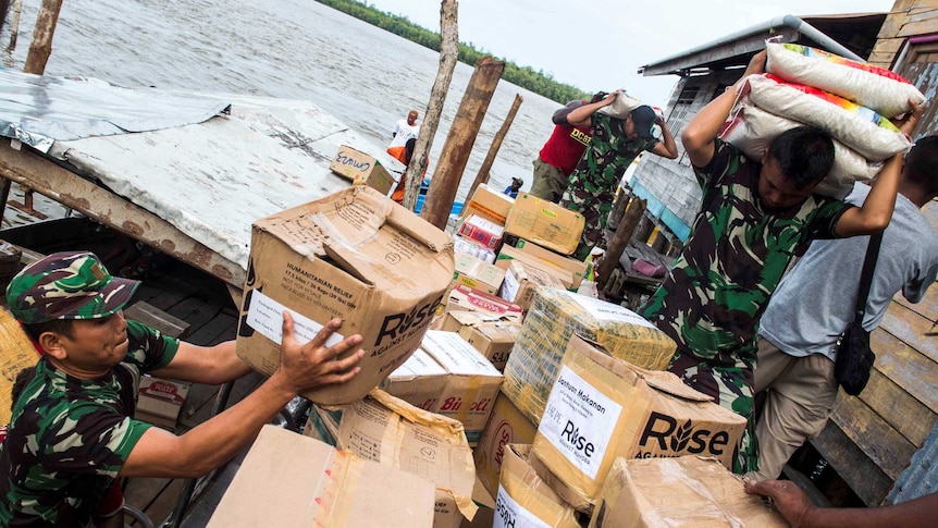 Indonesian soldiers carry rice and lift boxes as they unload supplies.