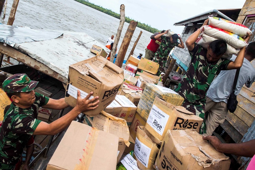 Indonesian soldiers carry rice and lift boxes as they unload supplies.