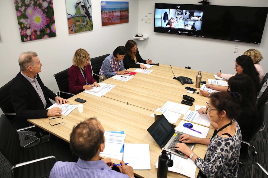 A group of people in a meeting room with a video conference underway.