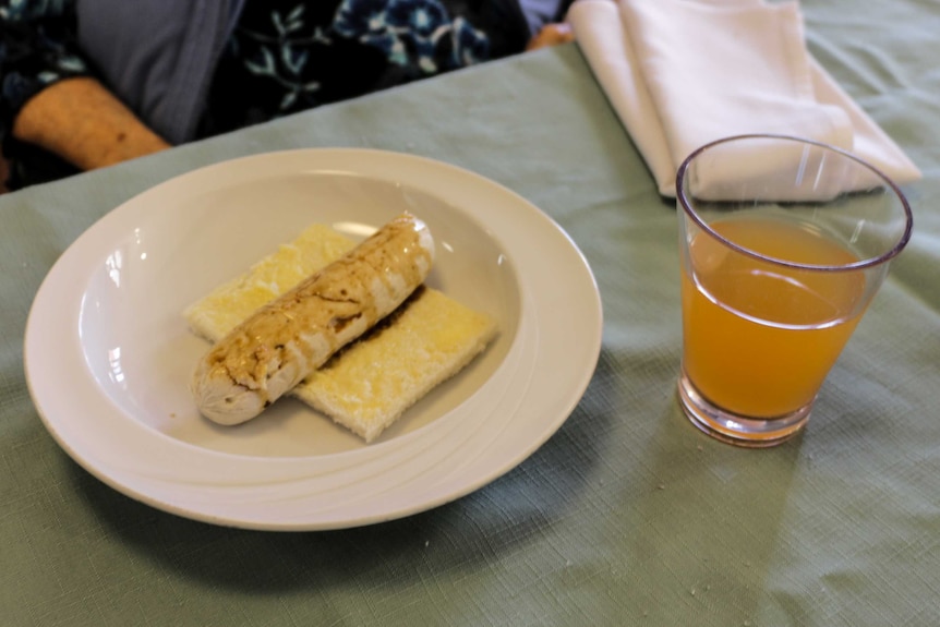The sausage invented by Lyndoch Living on a piece of bread next to a glass of orange cordial.