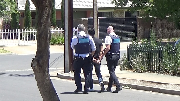 two police officers walking a man in handcuffs down a suburban street