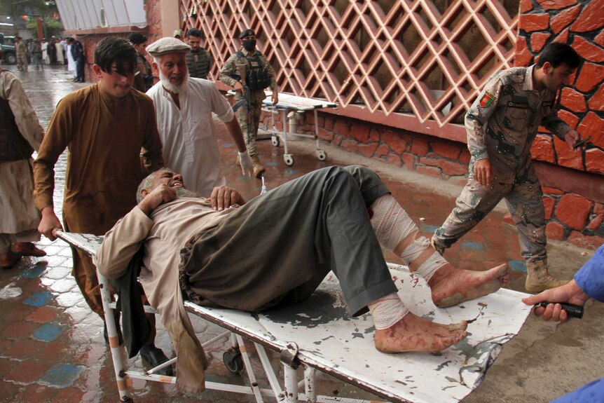 A man with a bandaged leg is carried on a stretcher into a hospital