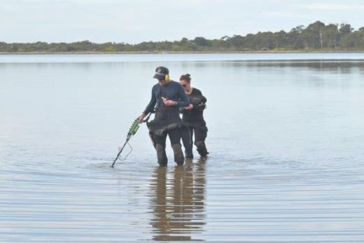 Two police, one male one female,  stand in the water using some kind of metal detector