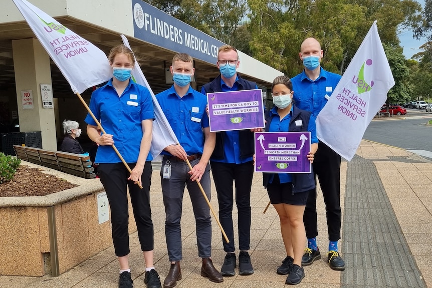 People wearing blue and holding purple placards outside a hospital