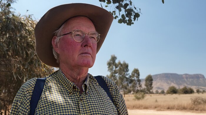 Wally Peart looks straight faced into the distance, with the mountain ranges behind him.