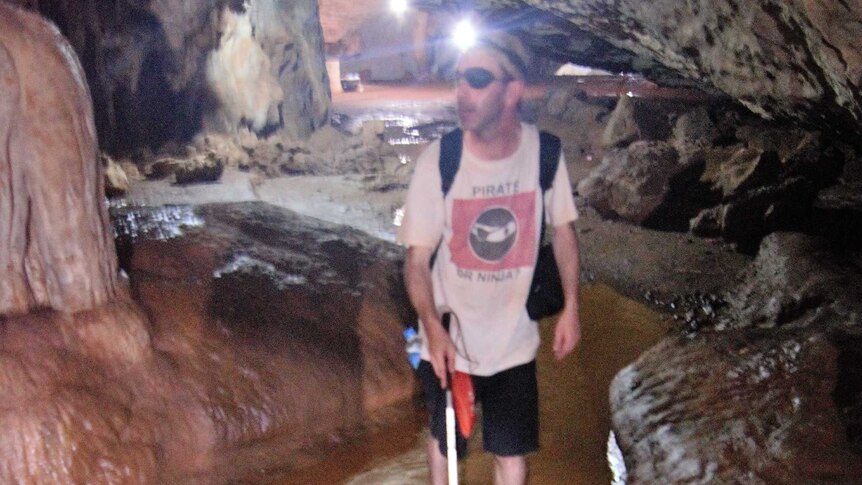 A man walks in shin-deep water, in a dark cave in Myanmar using a white cane for guidance