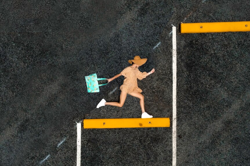 Photographed from above, a girl in a sundress and hat appears to be running up stairs on a black chalky background