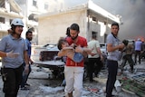 A man carries a young child away from fires and destroyed buildings left by a reported air strike in Idlib, Syria.