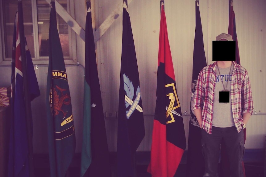 A man in casual dress stands in front of a row of flags