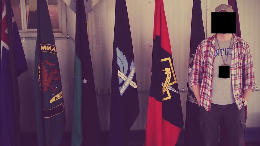 A man in casual dress stands in front of a row of flags
