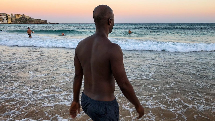 A man walking into the water at Bondi Beach.