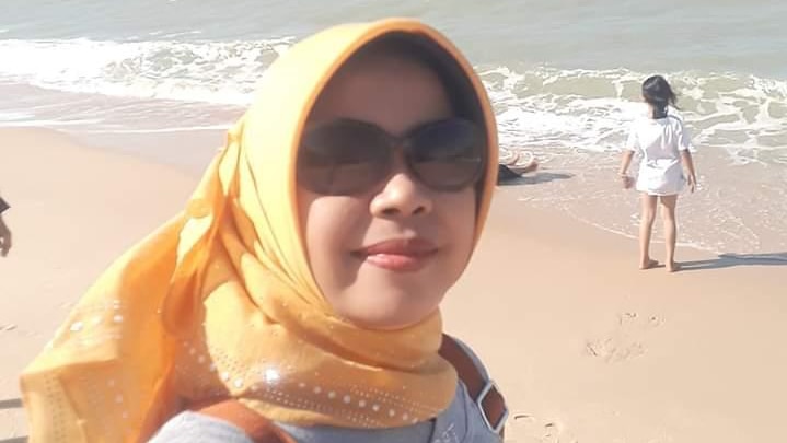 A woman in a headscarf takes a selfie on a beach
