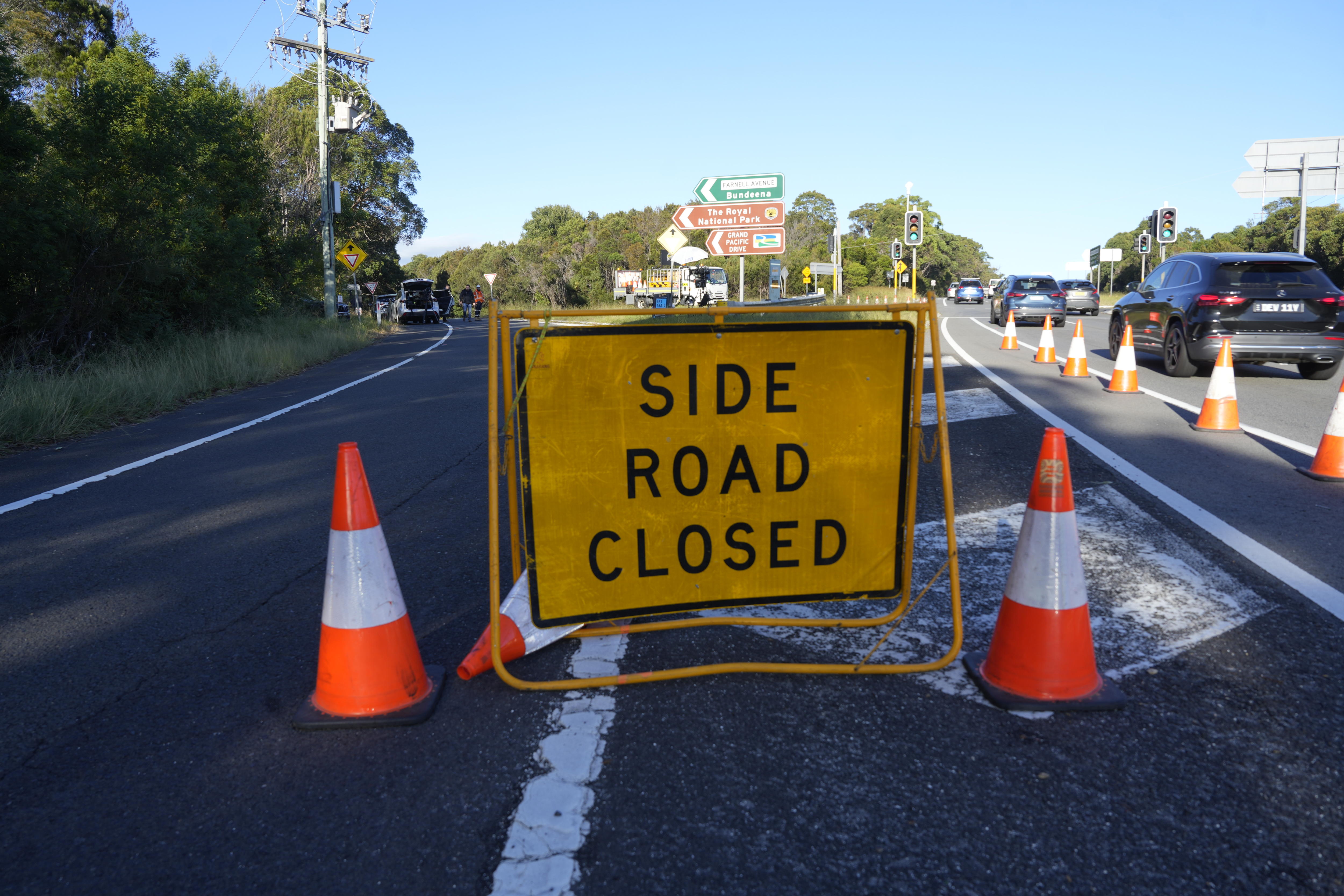A yellow road closed sign witth some orange cones around it and along the side of one road lane.