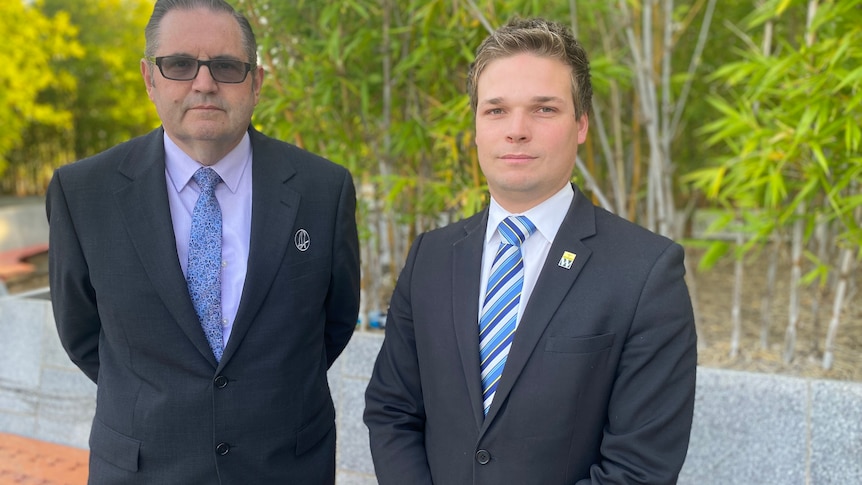 two men in suits, looking serious at camera 