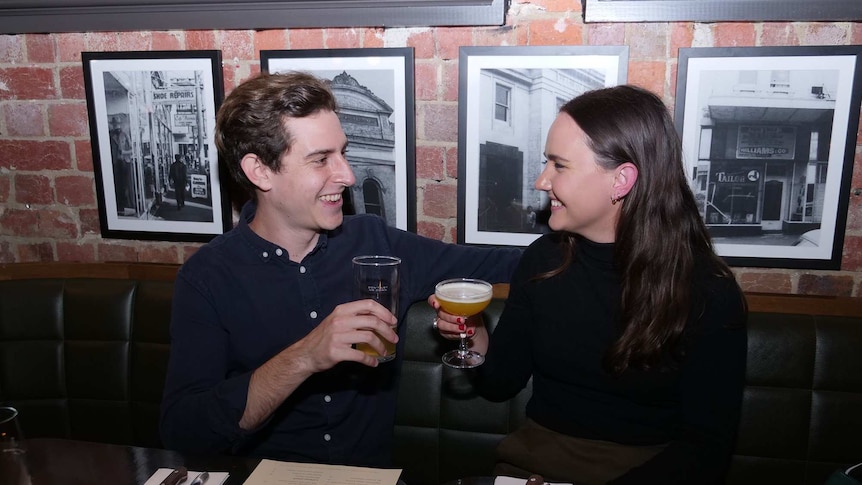 A young man and woman smile, with drink in hand