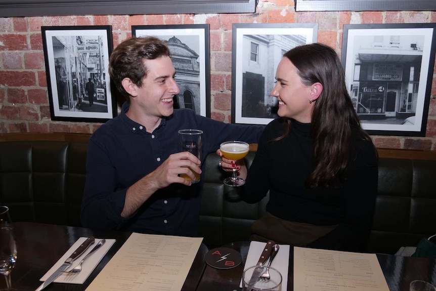 A young man and woman smile, with drink in hand