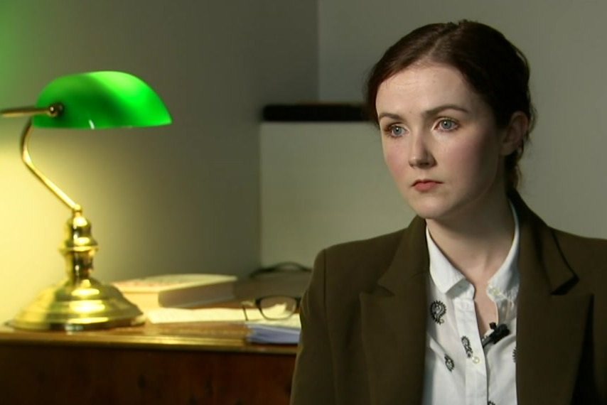 A woman sitting next to a green lamp.