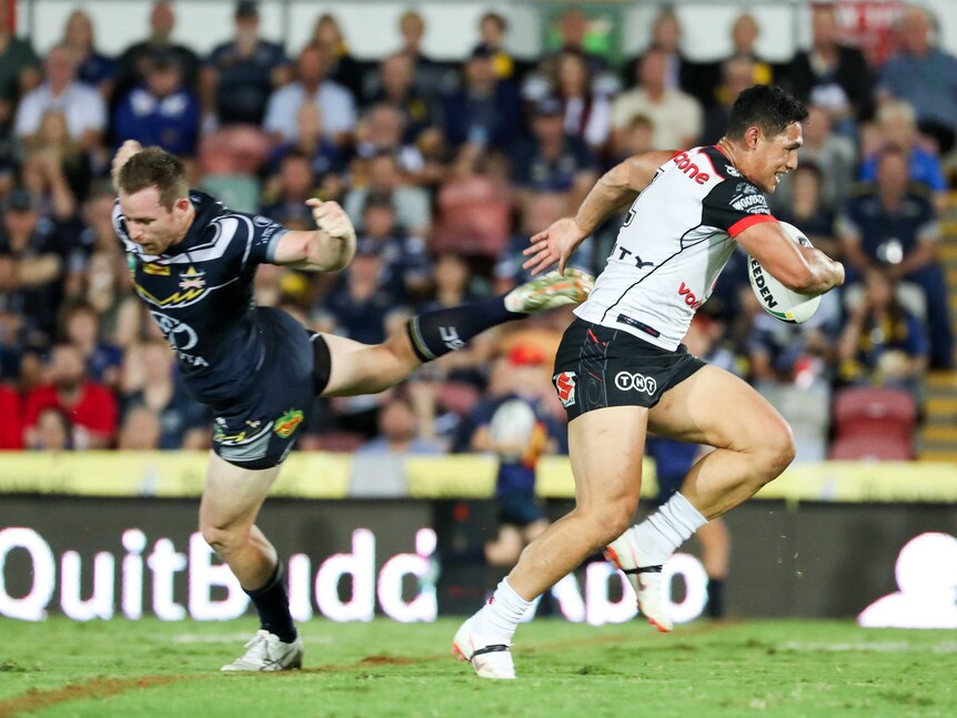 Roger Tuivasa-Sheck runs past Michael Morgan who has his arm outstretched and is falling forward.