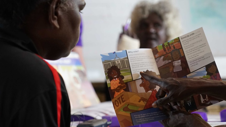 An Aboriginal woman points to a pamphlet on voting as another woman watches on.