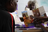 An Aboriginal woman points to a pamphlet on voting as another woman watches on.