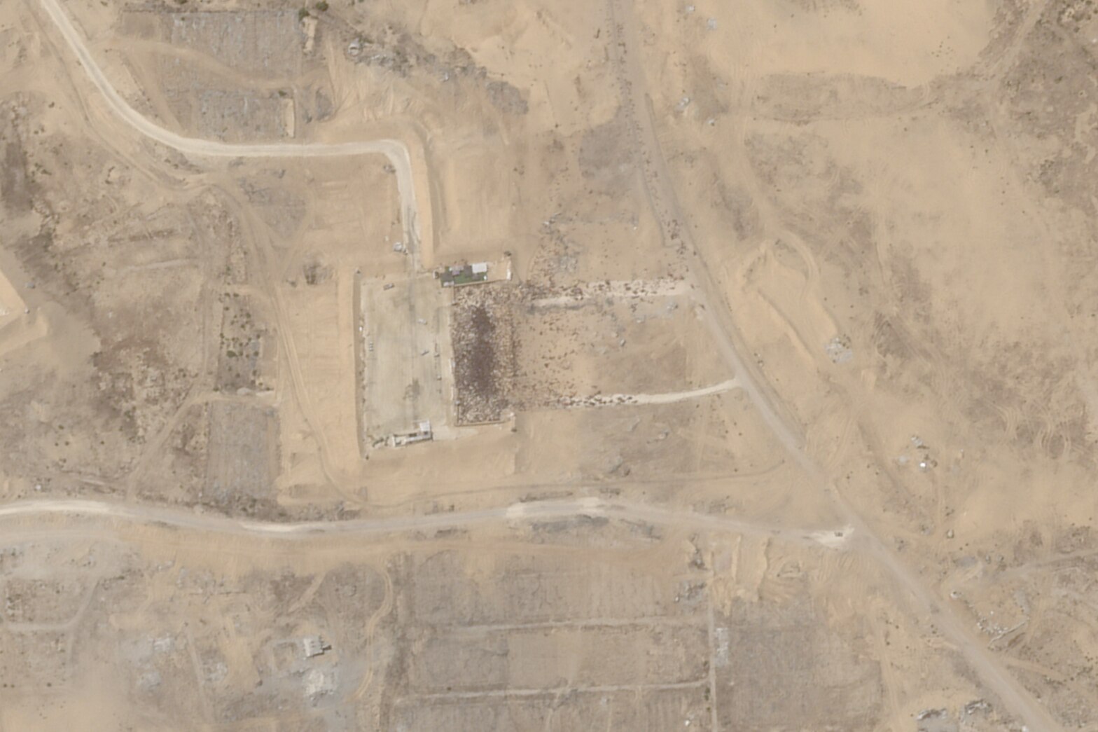 Satellite imagery shows a square aid centre etched into the dirt. Small black dots which are people are crowded around entrance