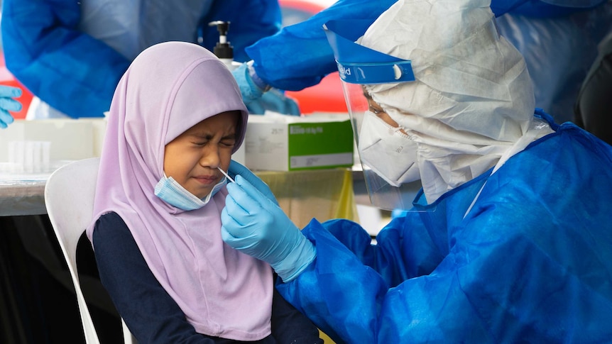 A doctor collects a sample for a coronavirus test from a Malaysian child