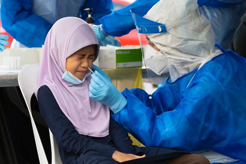 A doctor collects a sample for a coronavirus test from a Malaysian child