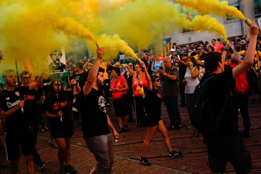 A group of Catalan pro-independence demonstrators holding yellow flares march past onlookers in Barcelona.