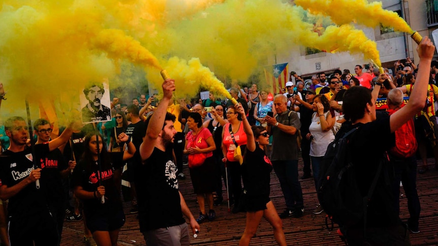 A group of Catalan pro-independence demonstrators holding yellow flares march past onlookers in Barcelona.