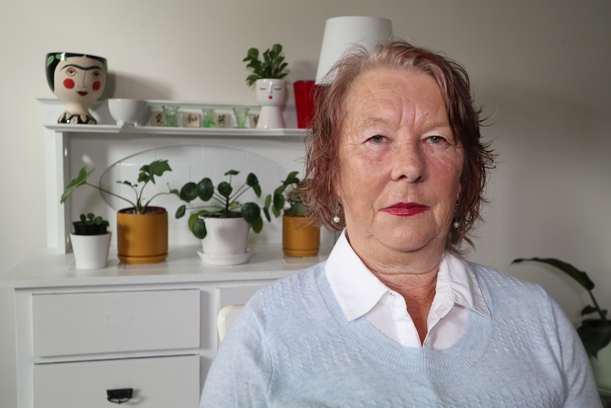 A woman wearing red lipstick sitting her home looks at the camera.