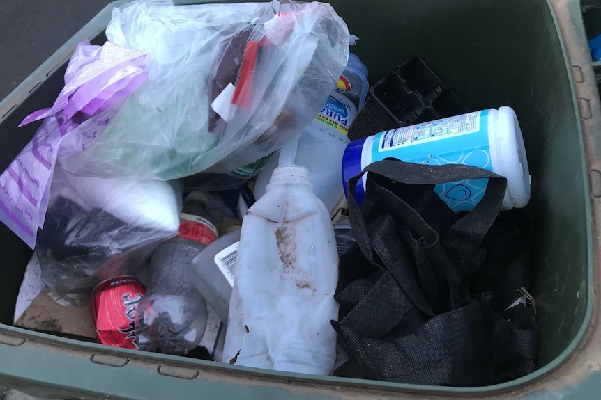 A rubbish bin with a mix of different kinds of waste, including plastic, cans and plastic bags.