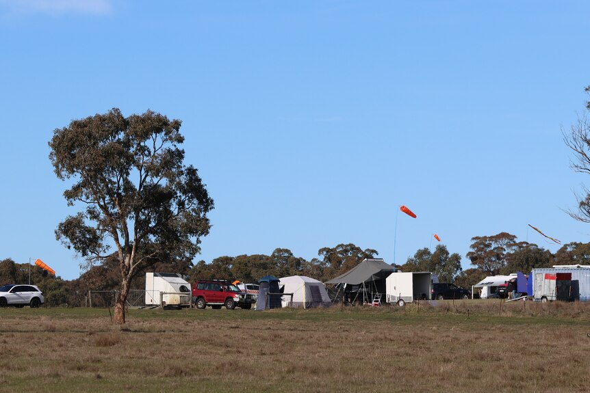 Wide image of an open field with tents and vehicles