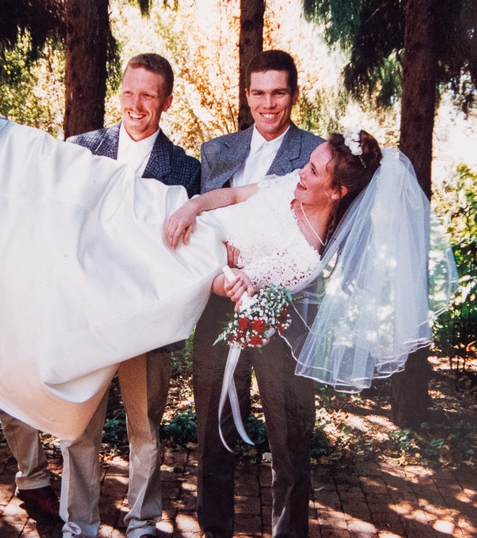 Three groomsmen pick up a smiling bride in a garden.