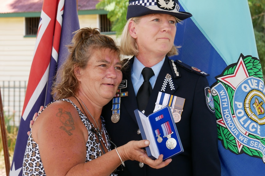 A woman holds a police medal in a velvet box open to the camera