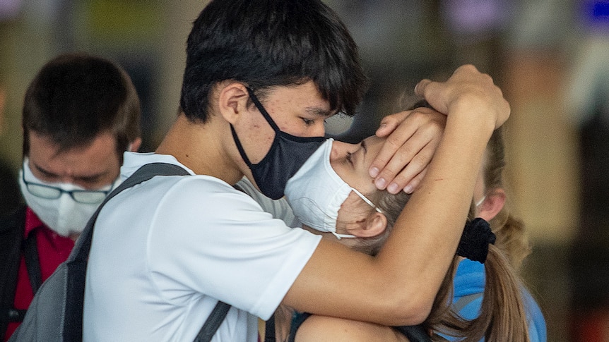 A young couple kisses each other at the airport wearing masks. 