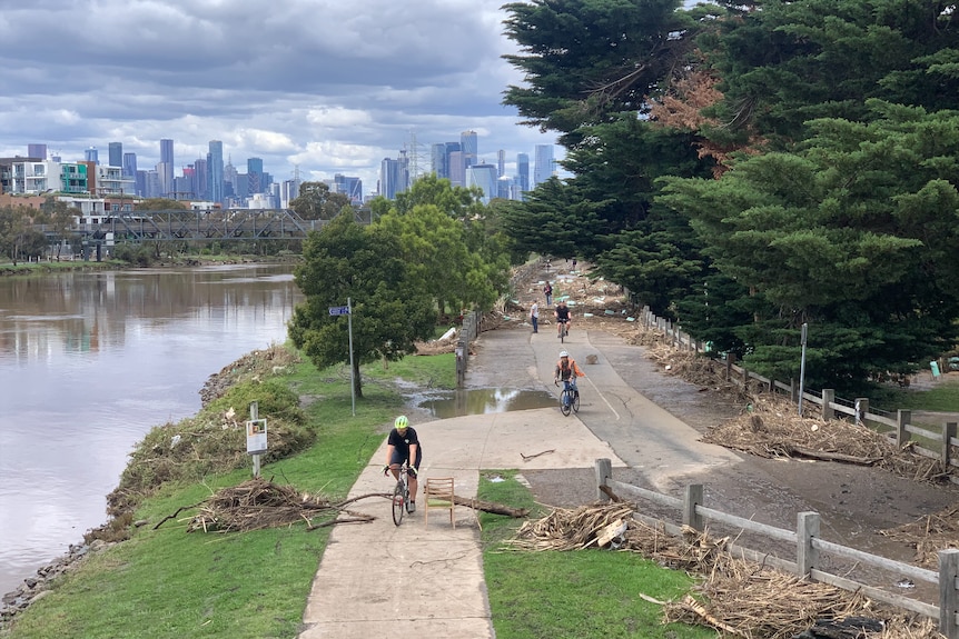 People cycling alongside a river, with debris over the path.