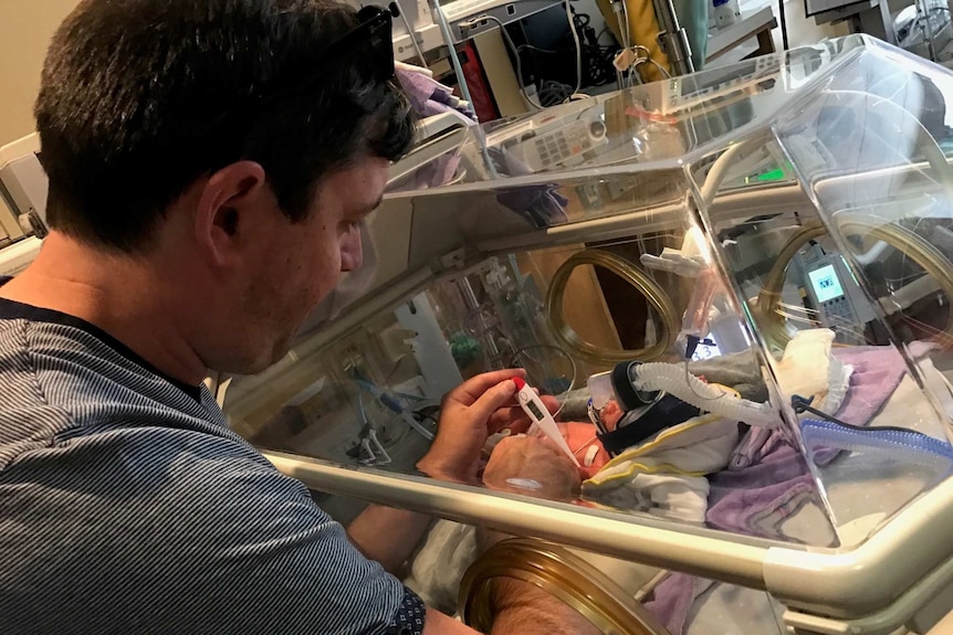 David Seddon stands next to his daughter who is in a crib for premature babies.
