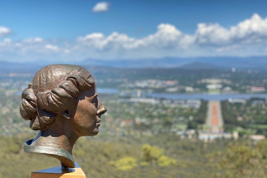 The bust of a statue of is attached to a lookout barrier, with Anzac Parade and Parliament House in the background.