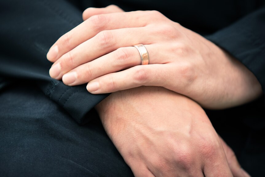 Hands resting on top of each other, with a silver and gold ring on the left hand.