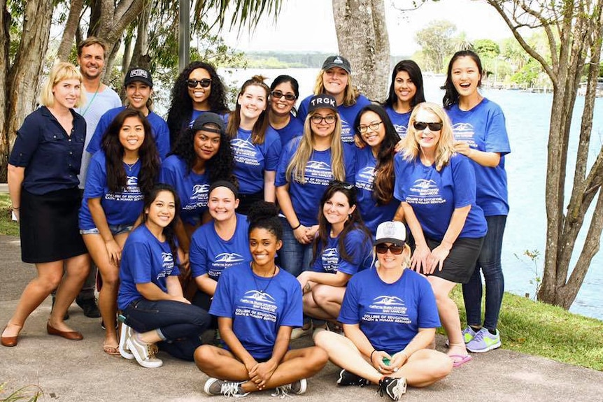 About 20 people stand as a group beside a river, happy and smiling. Volunteers wear blue shirts.