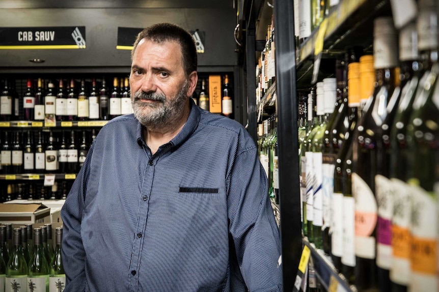 Un hombre parado junto al vino en una licorería.