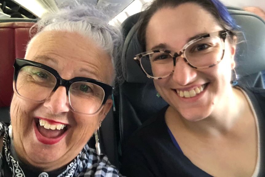 Two women smile sitting on a plane seat.