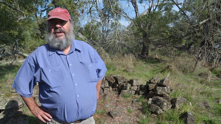 A man in a blue shirt and red hat stands in front of what looks like a pile of stones.