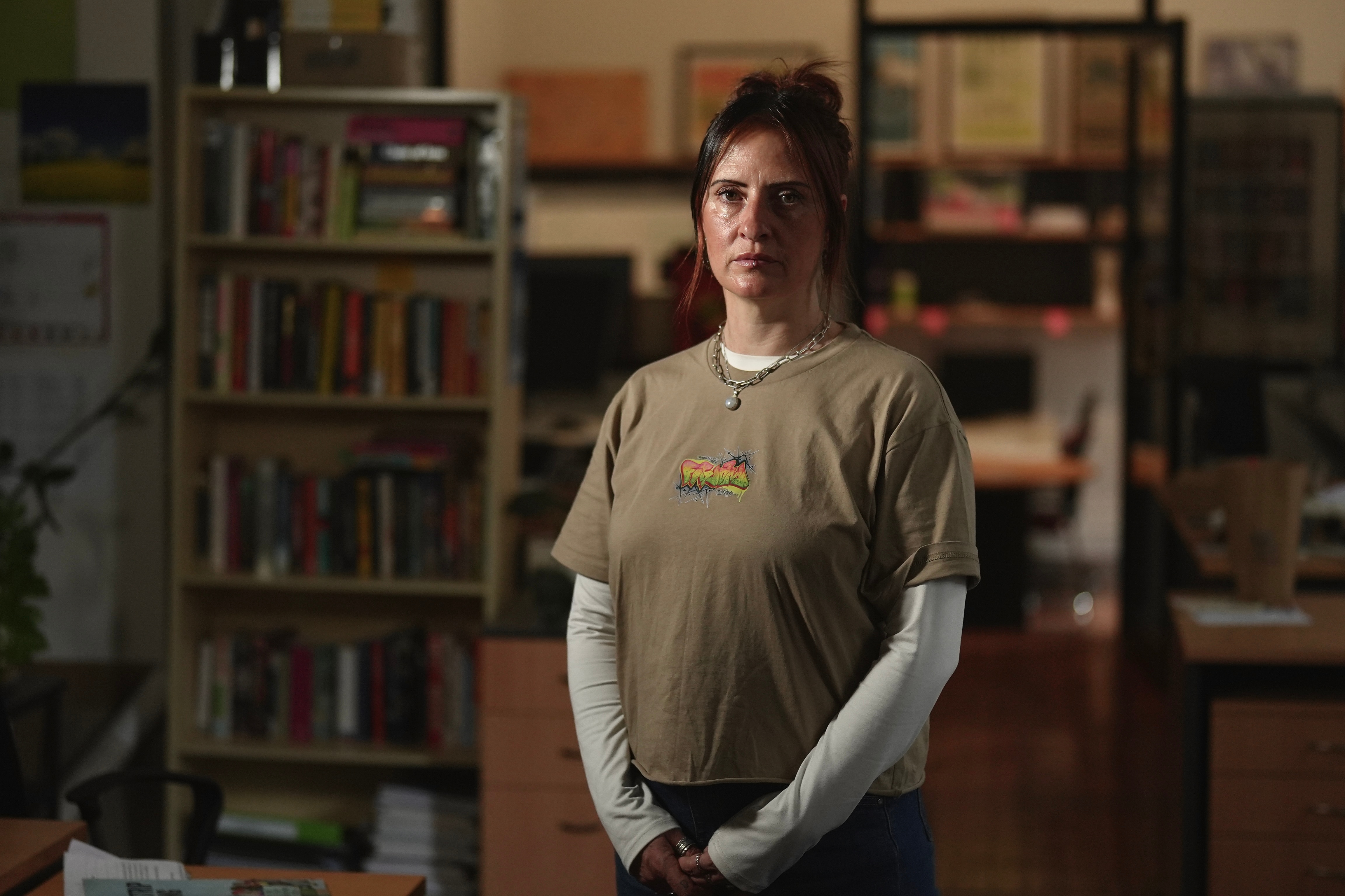 A woman with dark hair puled into a bun stands in a living room looking very serious.