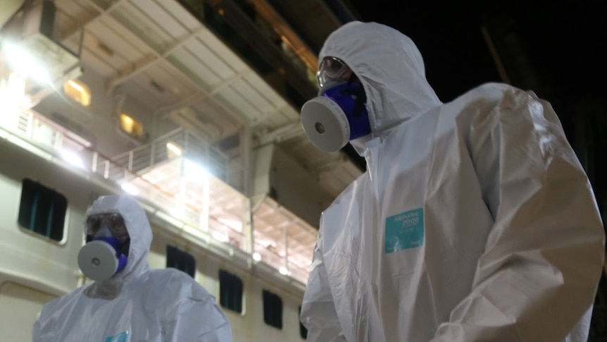 Two men in hazmat suits on a ship